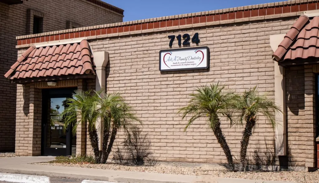 Exterior of brick dental office building: address “7124”, sign reading “Oral & Maxillofacial Surgery”, palm trees, tiled awning