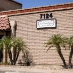 Exterior of brick dental office building: address “7124”, sign reading “Oral & Maxillofacial Surgery”, palm trees, tiled awning