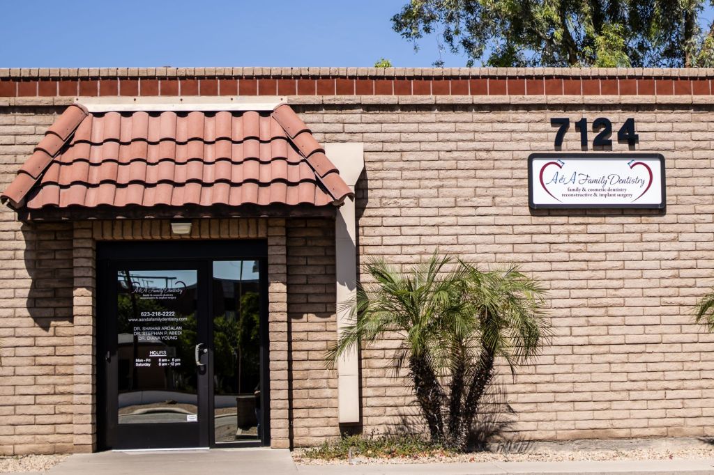 Exterior of brick dental office building: address “7124”, sign reading “Oral & Maxillofacial Surgery”, palm trees, tiled awning