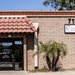 Exterior of brick dental office building: address “7124”, sign reading “Oral & Maxillofacial Surgery”, palm trees, tiled awning