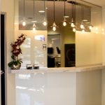 Modern dental reception desk with white glossy counter, hanging lights, and orchid arrangement