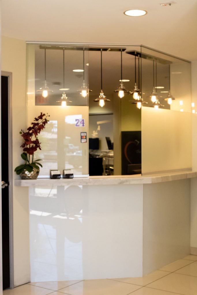 Modern dental reception desk with white glossy counter, hanging lights, and orchid arrangement