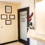 Dental office hallway with framed certificates, frosted glass door (logo visible), and orchid on counter