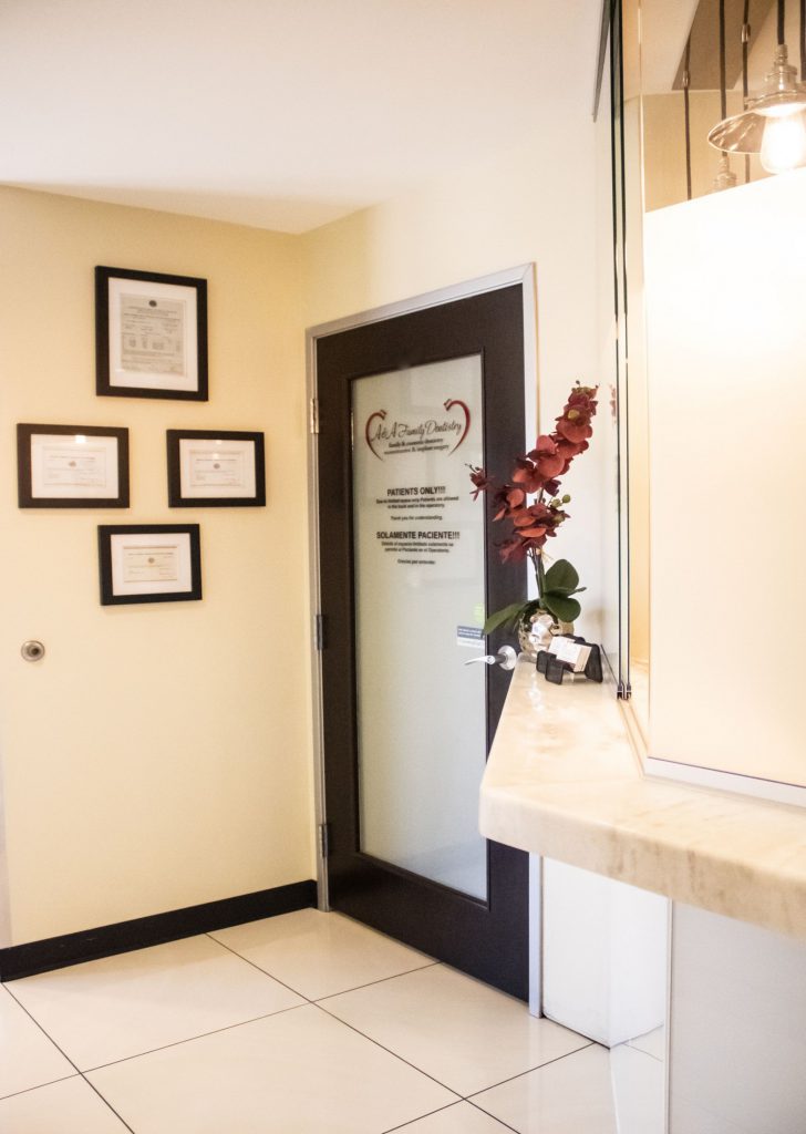 Dental office hallway with framed certificates, frosted glass door (logo visible), and orchid on counter