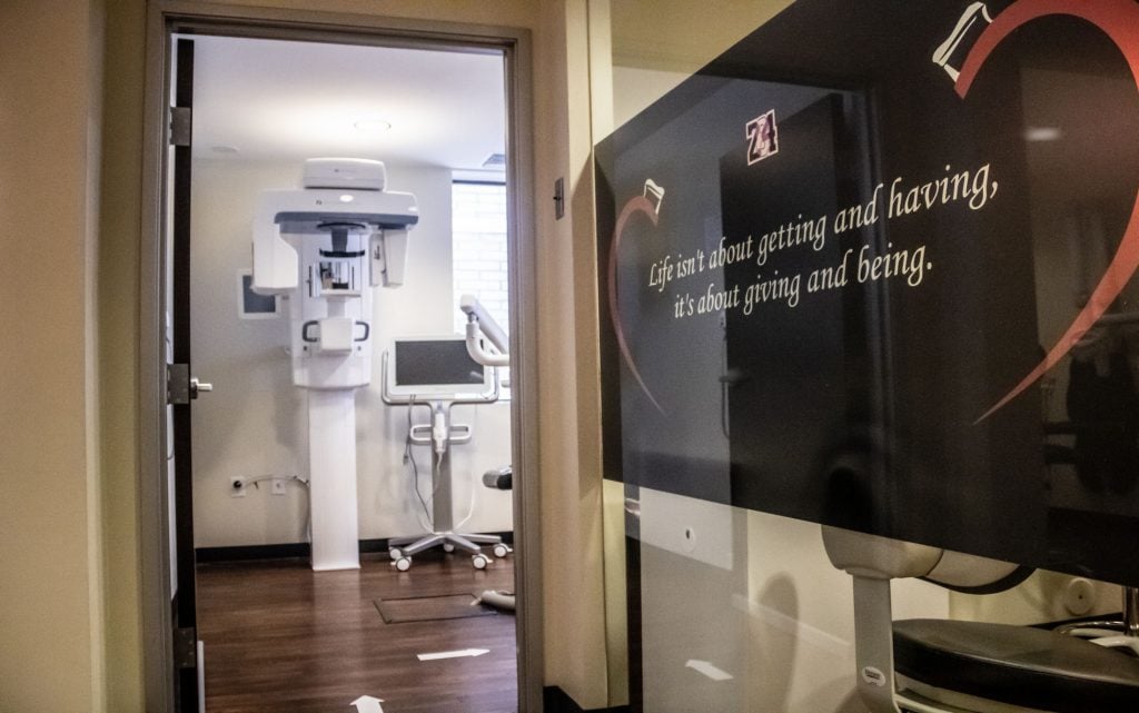 View through doorway into X-ray room with panoramic machine; adjacent wall displays same quote with heart graphic