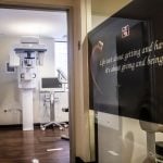 View through doorway into X-ray room with panoramic machine; adjacent wall displays same quote with heart graphic