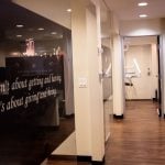 Dental treatment room with black chair, dual monitors, overhead light, and equipment