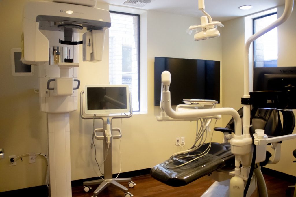 Dental treatment room with panoramic X-ray unit, dental chair, monitor, and overhead light