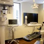 Dental treatment room with panoramic X-ray unit, dental chair, monitor, and overhead light
