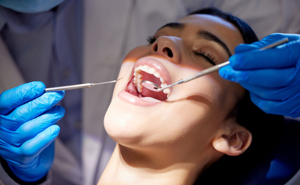 Close-up: clinician in blue gloves using mirror and probe to examine patient’s upper teeth
