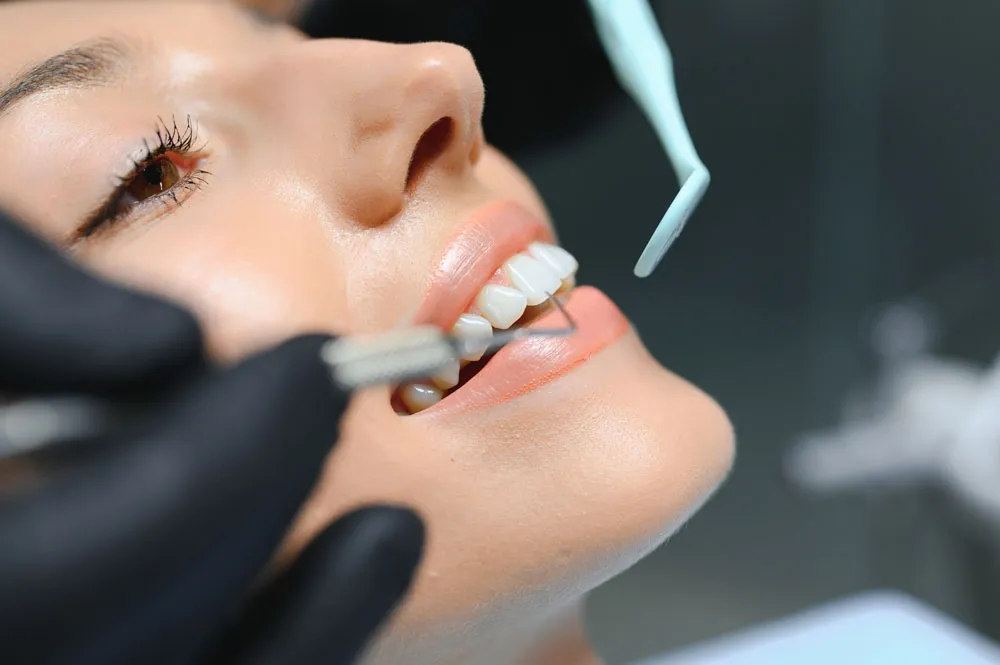 Extreme close-up: gloved hands using explorer and mirror on lower anterior teeth
